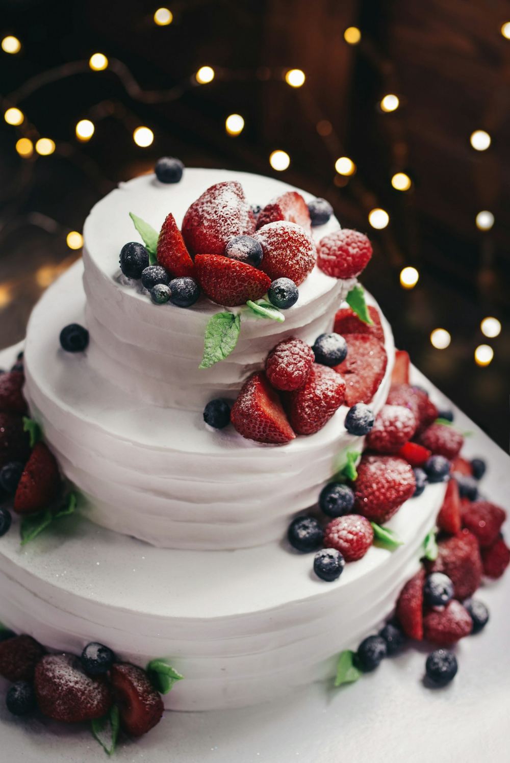 Bolo de festa de três andares, coberto de chantilly e decorado com morangos e mirtilos
