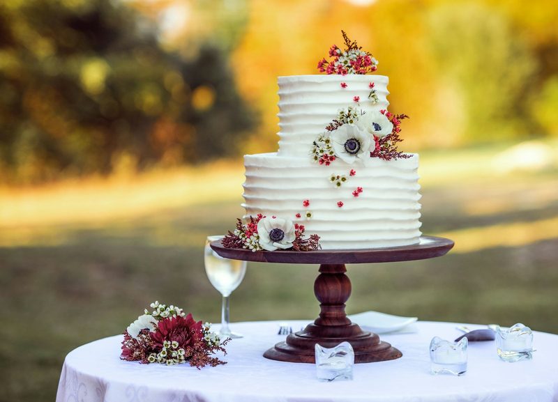 Bolo de dois andares com flores e frutas sobre um suporte de madeira