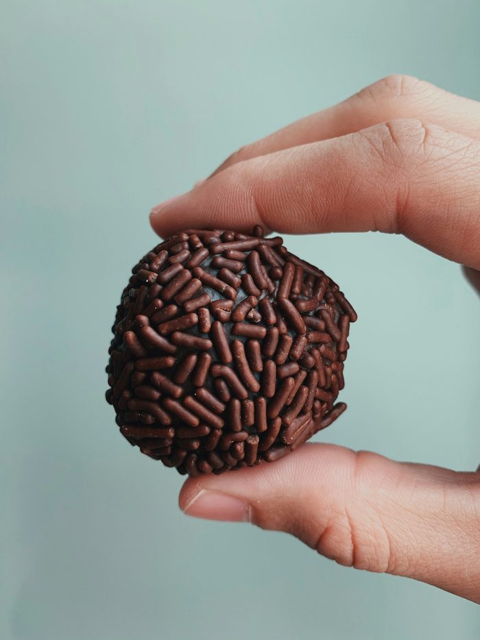 Mão segurando um brigadeiro grande coberto de granulado